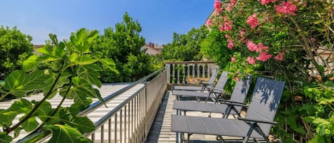 Una terraza en la azotea con barandilla de metal, una fila de sillones de descanso y vistas a zonas verdes y edificios.