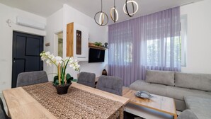Uma sala de estar moderna com uma mesa de jantar, sofás cinzas e uma TV fixada na parede.