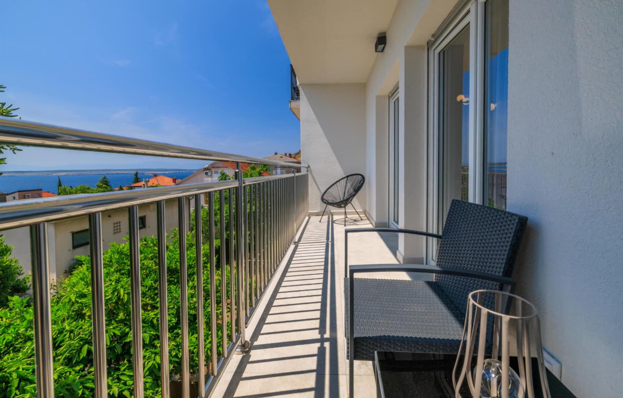 A balcony with a view of the sea, a chair, and a small table.