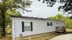 A single-story mobile home with a front porch, a small attached garage, and a pathway leading to the entrance.