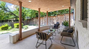 An outdoor patio with two wicker chairs and a small table, surrounded by a wooden pergola.