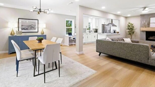Un salon moderne avec un canapé, une table à manger et des chaises. On aperçoit à l’arrière-plan un coin cuisine avec des placards et un plan de travail.