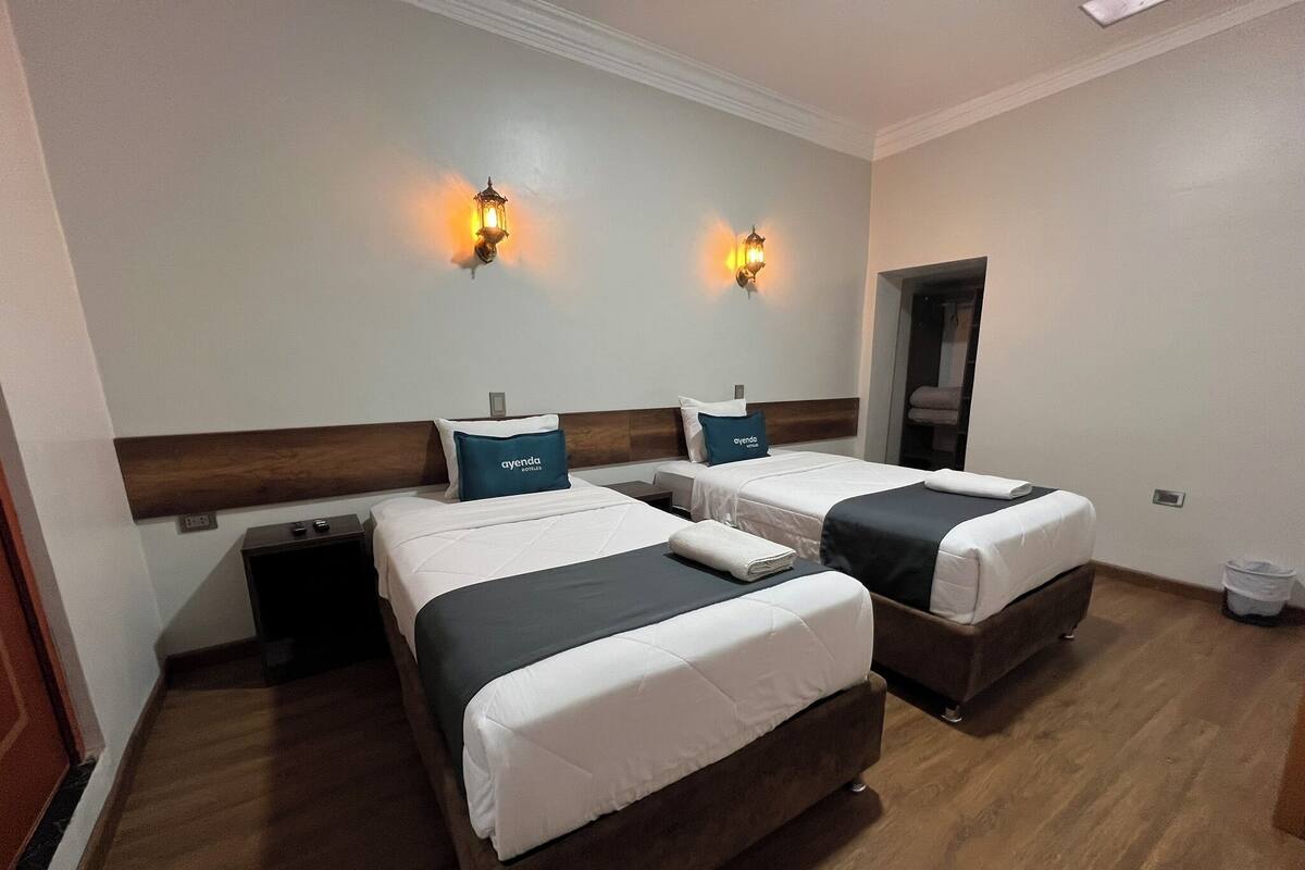 Ein Hotelzimmer mit zwei Betten, einem Holzkopfteil, einem Nachttisch und einer Wandleuchte.