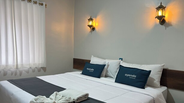Ein Hotelzimmer mit einem ordentlich bezogenen Bett, zwei Kissen mit dem Namen des Hotels, einem Bademantel auf dem Bett und zwei Wandleuchten.