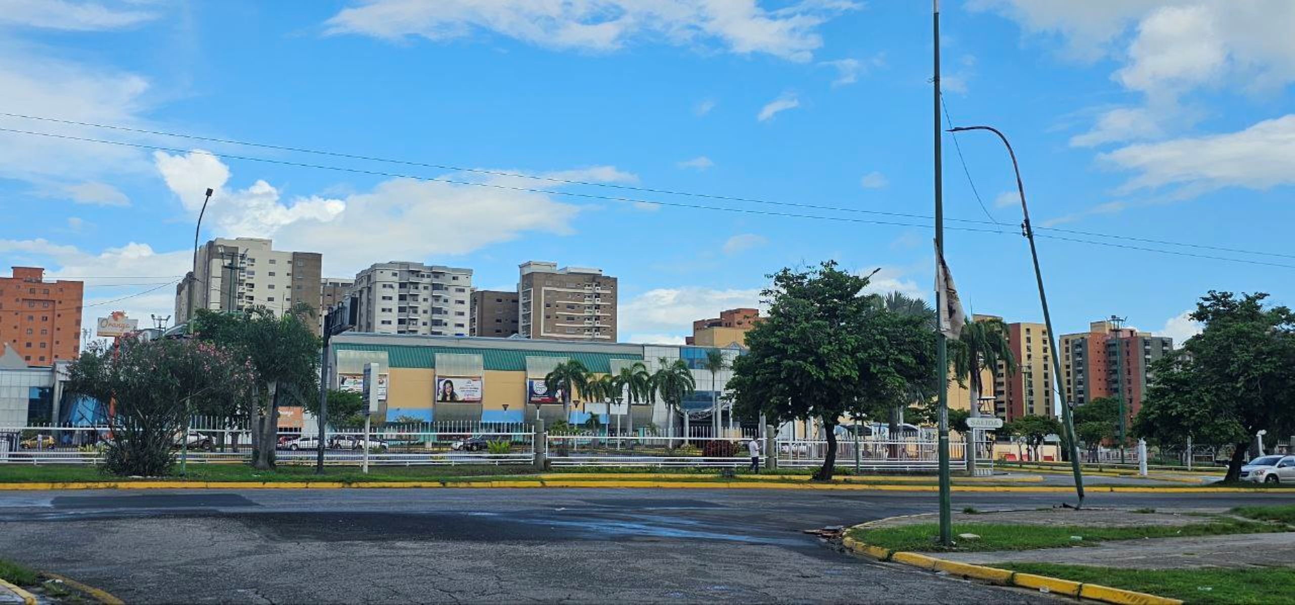 Un paisaje urbano con edificios modernos, cielo despejado y una calle con paso de peatones.