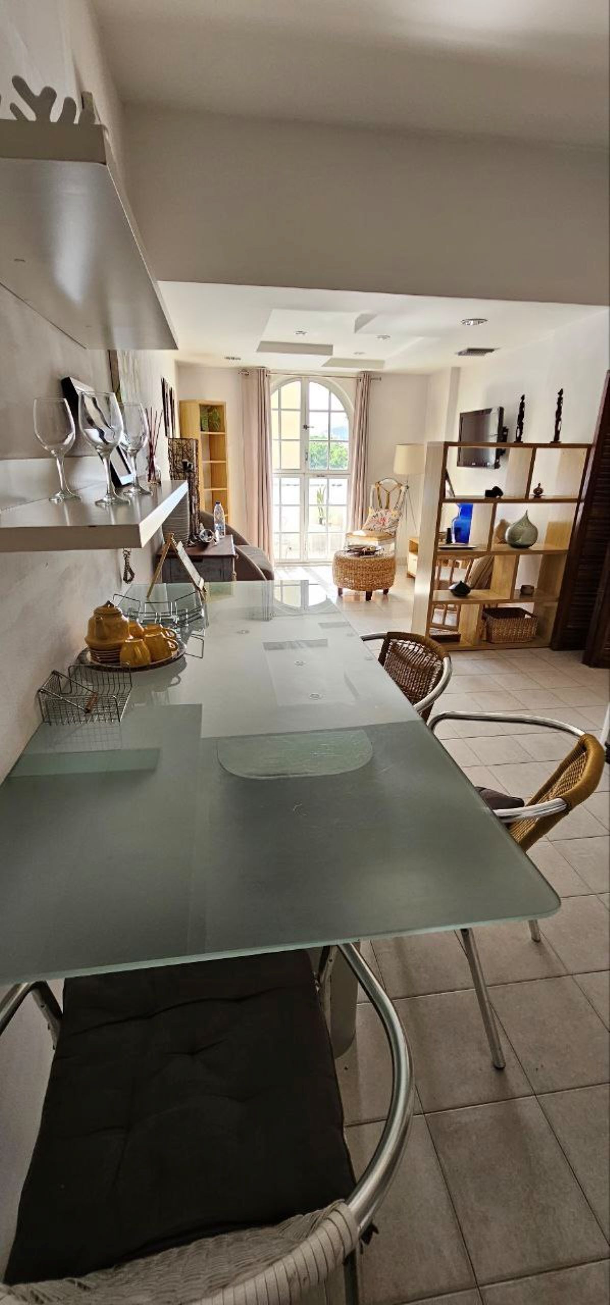 A modern dining area with a glass table, wicker chairs, and a view of the outdoors.