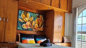 Un dormitorio con cama, armarios de madera, ventilador de techo y ventana grande.