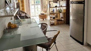 Una cocina moderna con una mesa de comedor de vidrio, sillas de mimbre, un refrigerador de acero inoxidable y vistas al exterior a través de amplias ventanas.