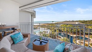 A balcony with a view of the sea, a pool, and a dining area with a table and chairs. - SeaCrest 2512 Stunning View, Walk to Coligny Shops & Restaurants (Hilton Head Island)