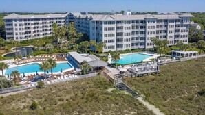 A multi-story hotel with a pool area, including a large pool and a smaller pool, surrounded by palm trees and lounge chairs. - SeaCrest 2512 Stunning View, Walk to Coligny Shops & Restaurants (Hilton Head Island)