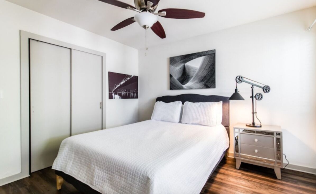 A bedroom with a bed, a ceiling fan, a nightstand, and a wall-mounted lamp.