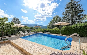 A swimming pool with lounge chairs and umbrellas, surrounded by greenery and mountains in the background. - Stunning home in Jurdani (Jurdani)