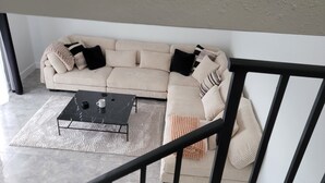 Una sala de estar moderna con un sofá modular, una mesa de centro y una escalera con barandillas negras.