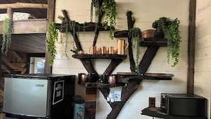 A kitchen with a refrigerator, a coffee maker, and shelves with plants and kitchenware.