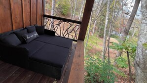 A wooden deck with a black sofa and cushions, overlooking a forested area.