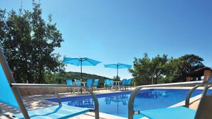 Zwembad met blauwe stoelen en parasols, omringd door bomen en een heldere lucht.