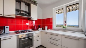 A modern kitchen with white cabinets, red tiles, a gas stove, an oven, and a window with a view of the landscape. - 1 bedroom cozy apartment in Sibenik (Sibenik)