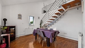 A spacious room with a wooden floor, a dining table with purple tablecloths, a staircase with wooden steps, and a radiator. - 1 bedroom cozy apartment in Sibenik (Sibenik)