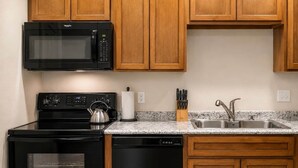 Een keuken met een fornuis, magnetron, spoelbak en houten keukenkastjes.