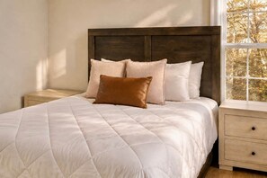 A bed with a quilted white duvet, a wooden headboard, and multiple pillows.