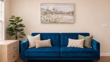 A blue sofa with four cushions, a wooden side table, and a large painting on the wall.