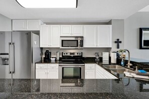 A modern kitchen with white cabinets, a stainless steel refrigerator, a microwave, a stove, and a sink with a faucet.