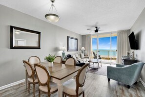 Uma sala de estar ampla com mesa de jantar, cadeiras, sofá e varanda com vista para o mar.