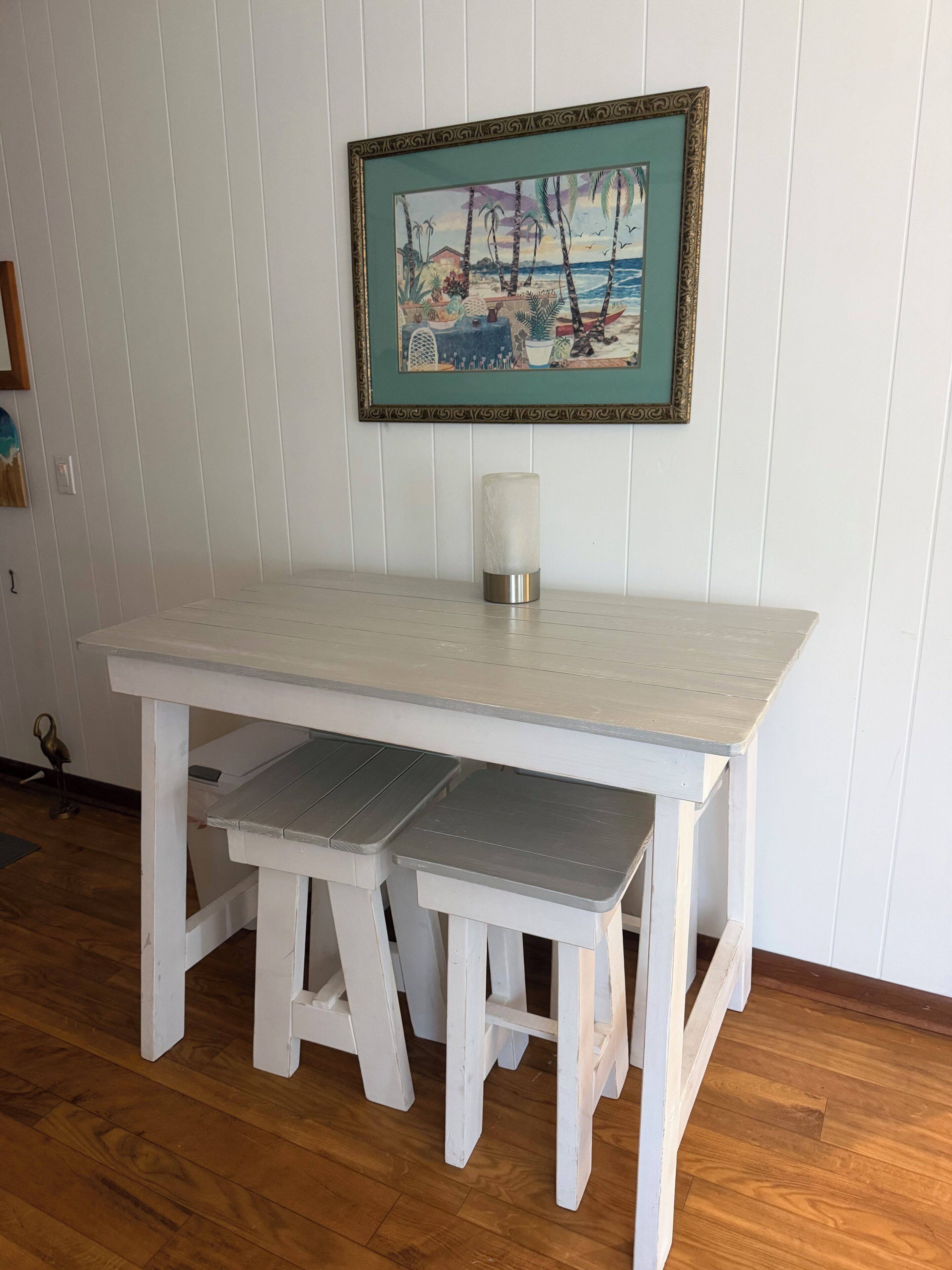 A white wooden table with a framed painting above it and a candle in the center.