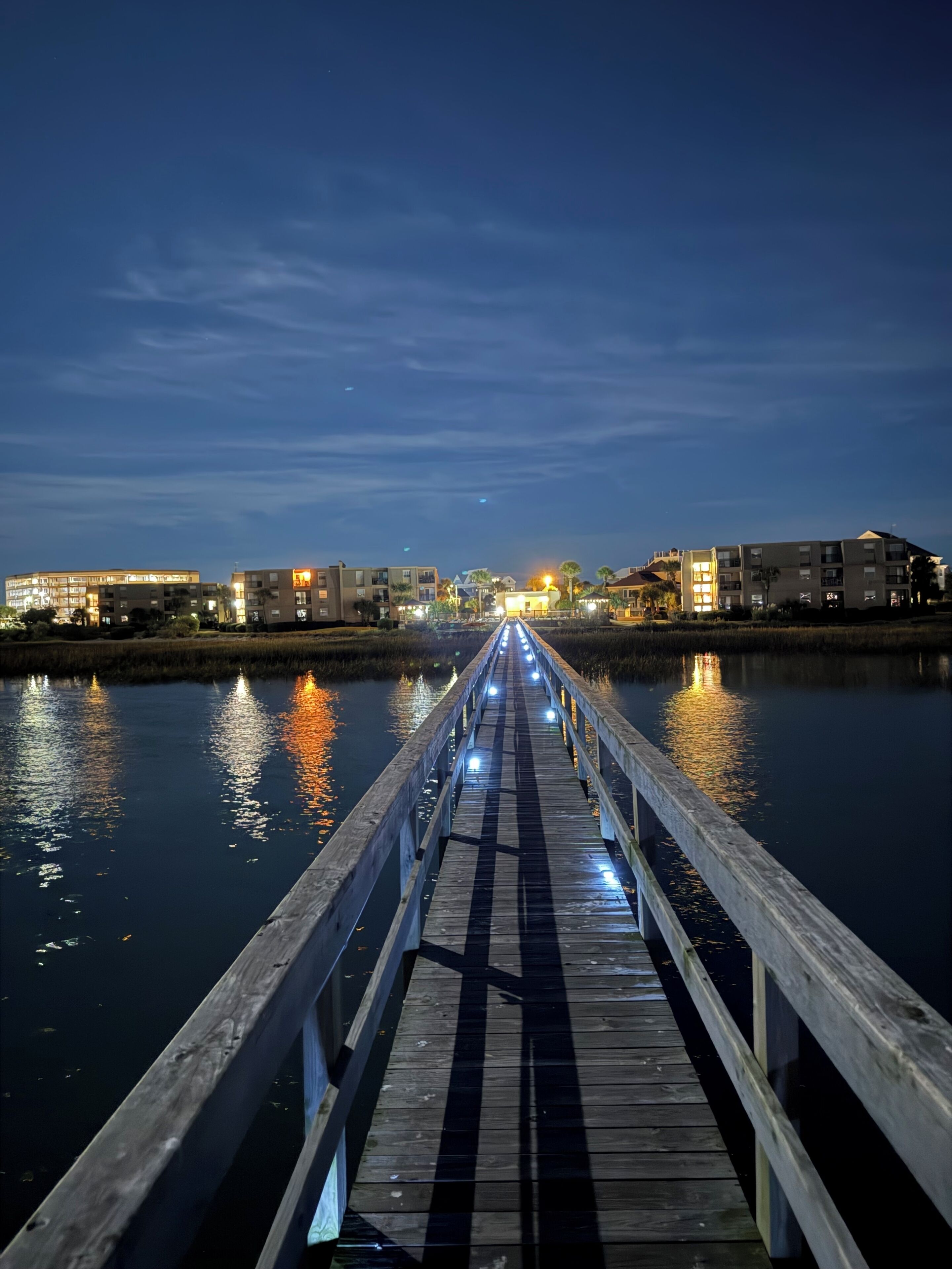 A wooden pier extending into calm water with buildings in the background.