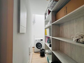 A laundry room with a washing machine, shelves with storage items, and a wooden floor. - Villa Nautica Puerto Rico by Alquiler de Súeño (Mogan)