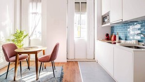 A compact kitchen with white cabinets, a blue backsplash, and a small dining area with two chairs and a table. - House Steps from Porto’s Best Attractions (Vila Nova de Gaia)