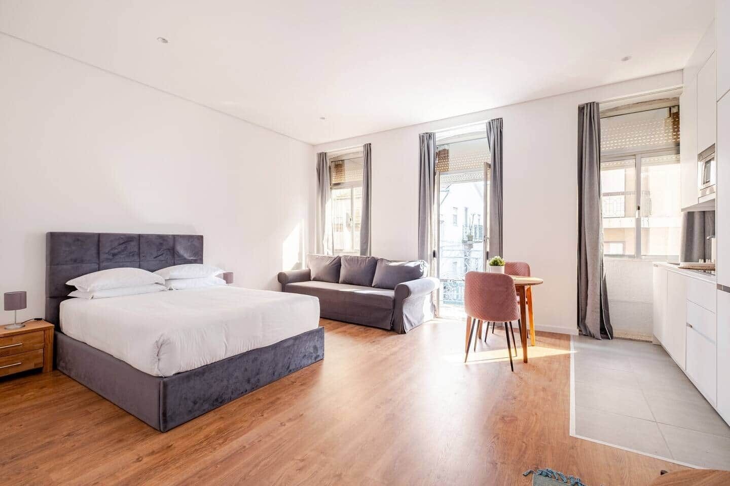 A modern hotel room with a large bed, a sofa, a dining area, and a kitchen.