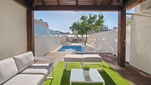 Un espace extérieur abrité doté d’une piscine, de mobilier blanc et d’une pelouse artificielle verte.