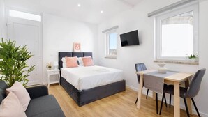 A modern bedroom with a bed, bedside table, TV, desk, chair, and a potted plant. - Riverside Studio By Luís Bridge, WOW & Half Rabbit (Vila Nova de Gaia)