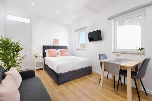 A modern bedroom with a bed, bedside table, TV, desk, chair, and a potted plant. - Riverside Studio By Luís Bridge, WOW & Half Rabbit (Vila Nova de Gaia)