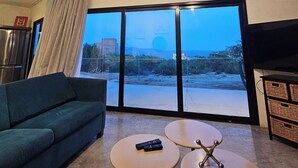 A living room with a sofa, two small tables, a TV, and a large sliding glass door leading to an outdoor area. - CASA ZORRO Close to the hot springs, bike trails and beautiful beach. (El Sargento)