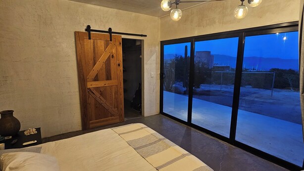 A bedroom with a large bed, a wooden door, a chandelier, and a view of the outside. - CASA ZORRO Close to the hot springs, bike trails and beautiful beach. (El Sargento)