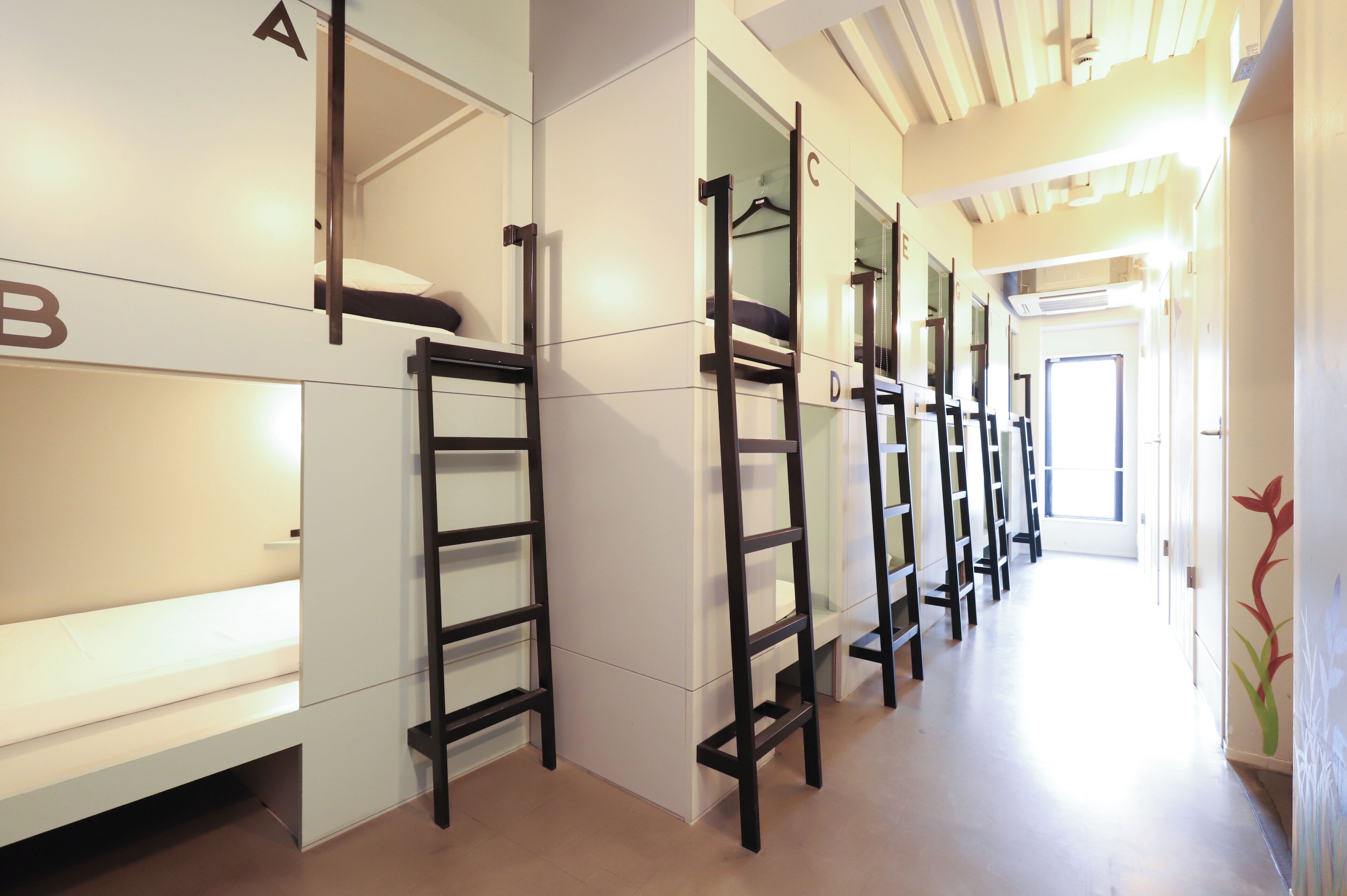 Camas individuales superpuestas con escaleras adosadas en un pasillo con piso de tonos claros y una puerta al final.