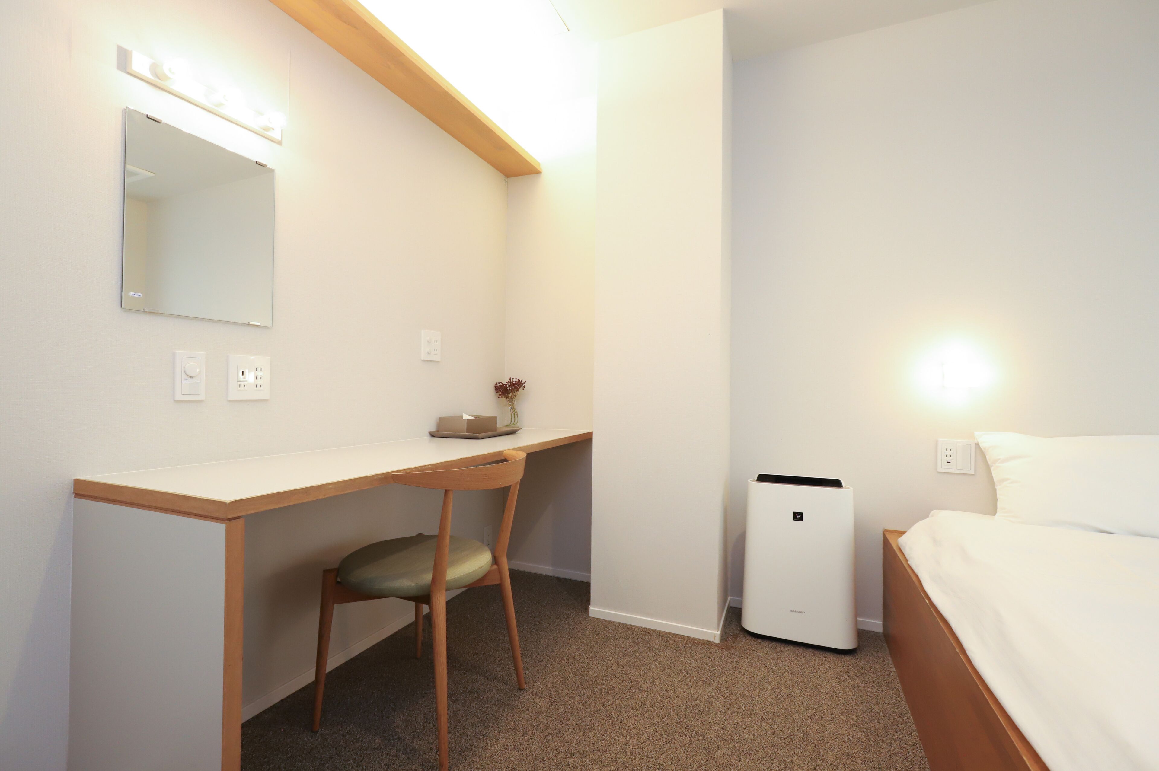A bedroom with a bed, a desk with a chair, a bedside table, a mirror, and a heater.