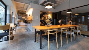 Een moderne eetruimte met een lange houten tafel en stoelen, een keuken op de achtergrond en een trap naar een hoger niveau.