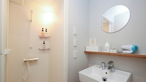 Een badkamer met een douche, wastafel en spiegel. Er liggen toiletartikelen op de wastafel en erboven een handdoekhouder.