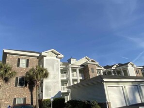 A multi-story residential building with a brick facade, white balconies, and a garage. - Stylish Condo at Myrtlewood Golf Overlooking Pool (Myrtle Beach)