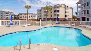 A swimming pool with a 5 ft depth marker, surrounded by lounge chairs and a white fence. - Myrtlewood Retreat Near Golf & Ocean Breezes | Magnolia Pointe Luster Leaf 4890-205 (Myrtle Beach)