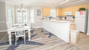 A modern kitchen with white cabinetry, a central island, and a dining area with a white table and chairs. - Myrtlewood Retreat Near Golf & Ocean Breezes | Magnolia Pointe Luster Leaf 4890-205 (Myrtle Beach)