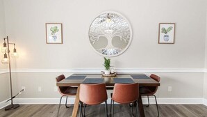 A dining area with a round table, four chairs, and a decorative tree wall art piece.