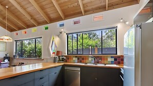 A modern kitchen with wooden beams, large windows, and a colorful backsplash. - Peaceful, creative home in a lush
bush setting, only 300m from the beach! (Skenes Creek)