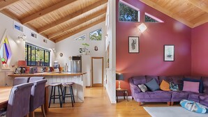 A spacious living area with a wooden ceiling, a purple sofa, and a dining area with wooden furniture. - Peaceful, creative home in a lush
bush setting, only 300m from the beach! (Skenes Creek)