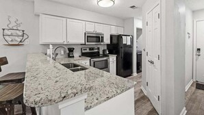 A modern kitchen with white cabinets, a granite countertop, stainless steel appliances, and a wooden dining table.