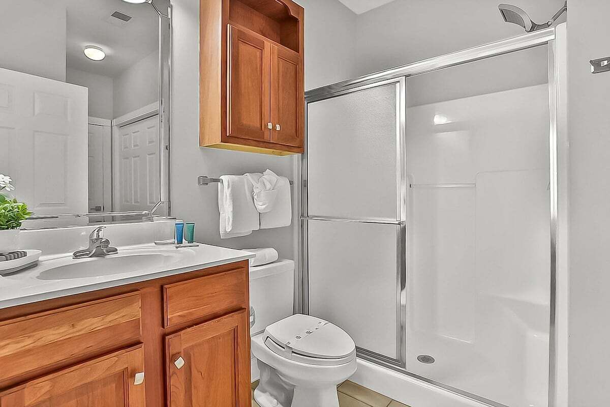 A bathroom with a shower, toilet, sink, and wooden cabinets.