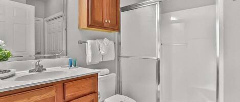 A bathroom with a shower, toilet, sink, and wooden cabinets.